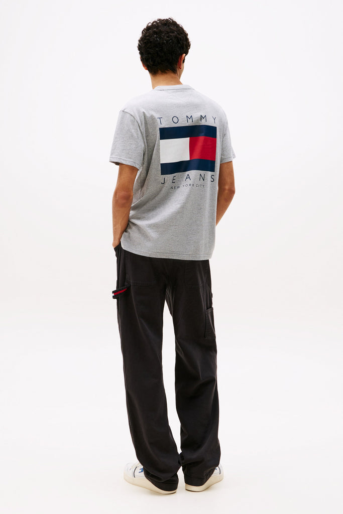Person wearing a Tommy Jeans t-shirt with a flag logo on the back, standing against a white background.